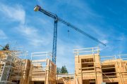 A crane constructs a low-rise wooden building under sunny skies in British Columbia.